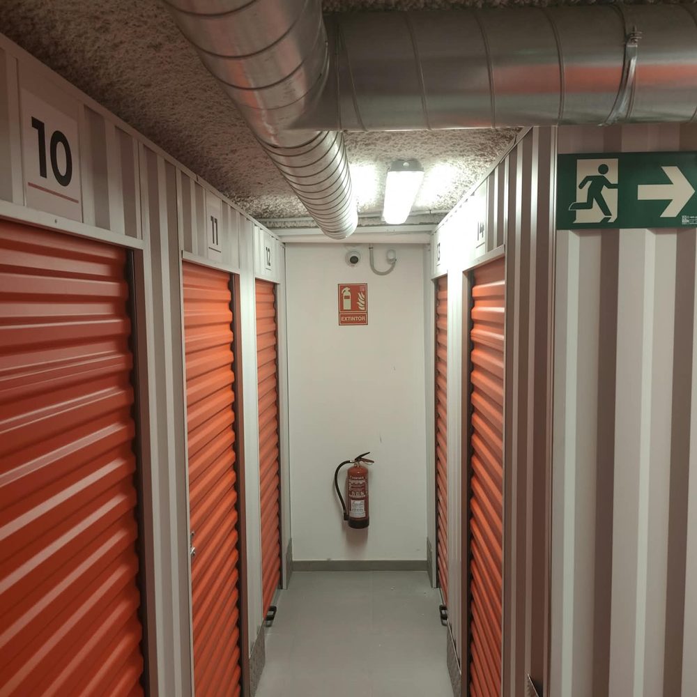 Pasillo de trasteros en la Eixereta con extintor y salida de emergencia señalizada